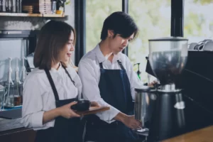 Two baristas, one male one female, working behind the counter in a coffee shop.