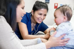 Female doctor checking a baby's chest with a stethoscope while the baby's mother holds her child.